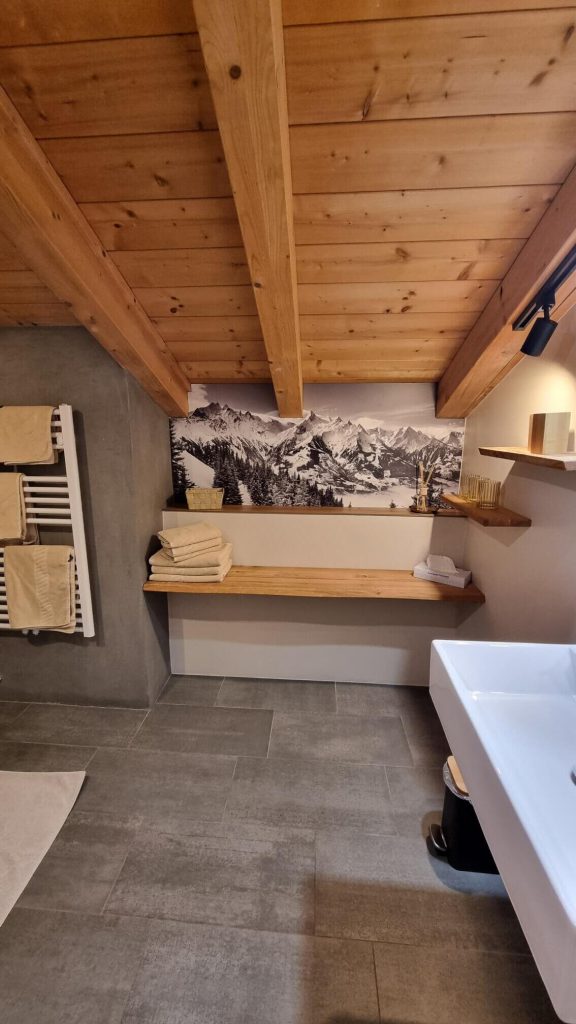 Gemütliches Bad mit Holzdecke, modernen Fliesen und Blick auf die Berglandschaft.