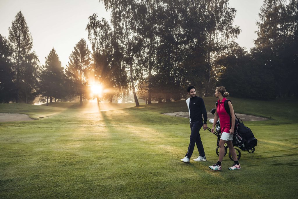 Paar beim Golfen in der Morgensonne auf einer weiten, grünen Wiese.